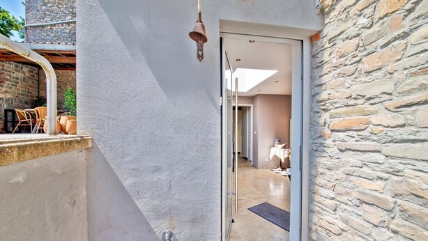 Un estrecho pasillo exterior con un muro de piedra en un lado y una puerta de cristal que da a un espacio interior.