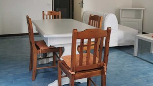 Zona pranzo con tavolo bianco e sedie di legno, un divano bianco e un tavolino bianco.