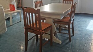 Un'area pranzo con un tavolo bianco e quattro sedie di legno, un armadietto bianco con una finestra e un pavimento piastrellato di blu.