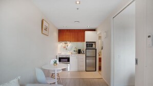 A modern kitchen with white cabinetry, a microwave, and a refrigerator. There is a dining area with a white table and chairs. - Quayside Quarters Apt close to Spark Arena (Auckland CBD)