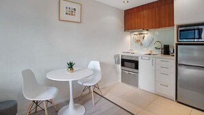 A modern kitchen with white cabinets, a stainless steel refrigerator, and a dining area with a white table and chairs. - Quayside Quarters Apt close to Spark Arena (Auckland CBD)