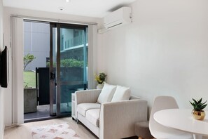 Un salon moderne doté d’une porte-fenêtre coulissante donnant sur un balcon, d’un canapé blanc, d’une petite table ronde et d’une plante en pot.