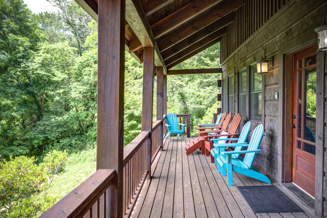 A wooden deck with Adirondack chairs and a wooden railing overlooking a forested area.