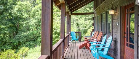 A wooden deck with Adirondack chairs and a wooden railing overlooking a forested area.