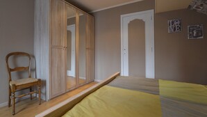 A bedroom with a bed, a wooden wardrobe, a chair, and a door. - Waimes Retreat Near Forest (Waimes)