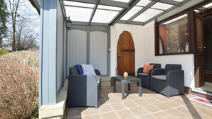 A covered patio area with two wicker sofas, a small table, and a wooden door. - Waimes Retreat Near Forest (Waimes)