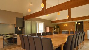 A spacious dining area with a long wooden table and modern chairs, a kitchen with a stove and refrigerator, and wooden beams on the ceiling. - Wellness & Wilderness: Libômont Escape (Waimes)