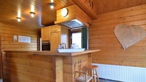 L’intérieur d’un chalet en bois comprend un coin cuisine, un élément décoratif mural en forme de cœur et un tabouret de bar en bois.