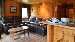 L’intérieur chaleureux d’un chalet, avec un revêtement mural en bois, un ensemble de canapés, une table basse et un coin cuisine équipé d’un évier et d’un plan de travail.
