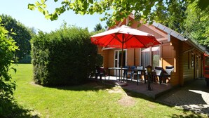 Une cabane en bois dotée d’un patio comprenant un espace salon extérieur et un parasol rouge.