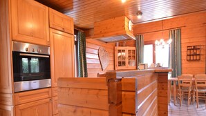 L’intérieur d’un chalet en bois comprend un coin cuisine équipé d’un four Bosch, une table à manger avec des chaises et un petit coin bar.