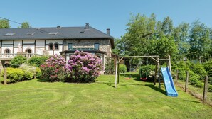 Et hus med en stenfacade, en stor have med gyngestativ og rutschebane, og en klar blå himmel.