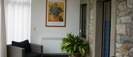 A living room with a wicker sofa, a red throw pillow, a potted plant, a framed artwork, and a stone wall.