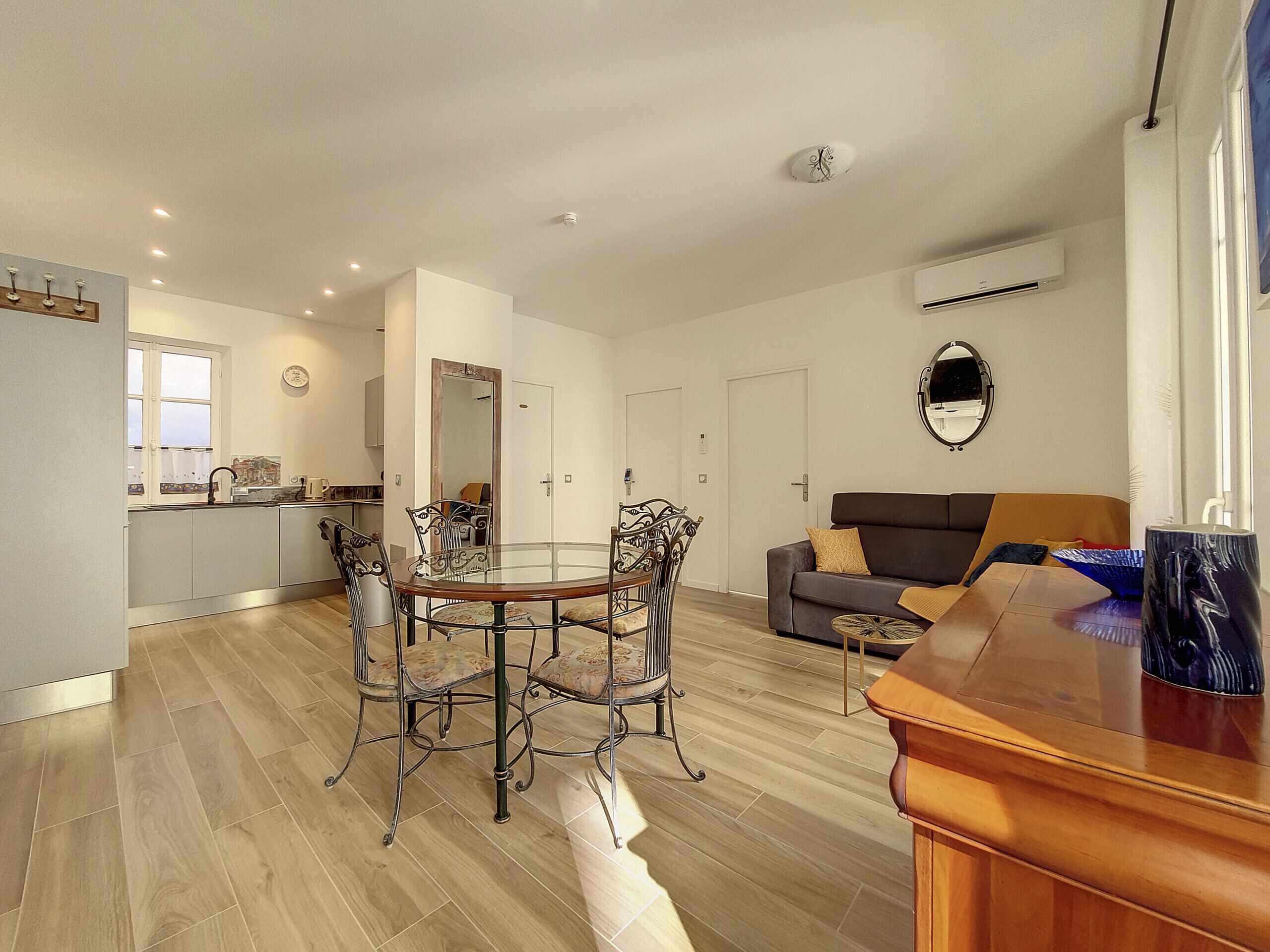 A modern kitchen with a dining area, a sofa, and a mirror.