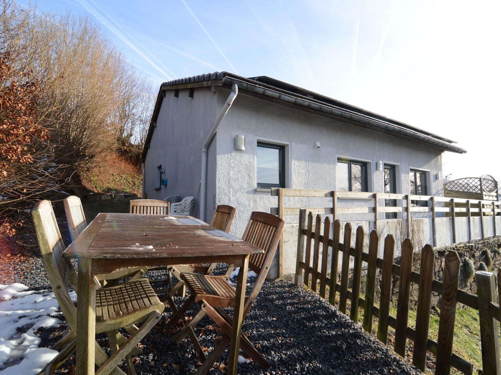 Une maison de campagne avec une table et des chaises en bois à l’extérieur, une allée en gravier et une clôture en bois.
