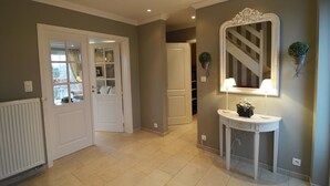 A hallway with a white door, a white console table with a mirror and lamps, and a radiator on the left. - Forestside Retreat, Malmedy (Malmedy)