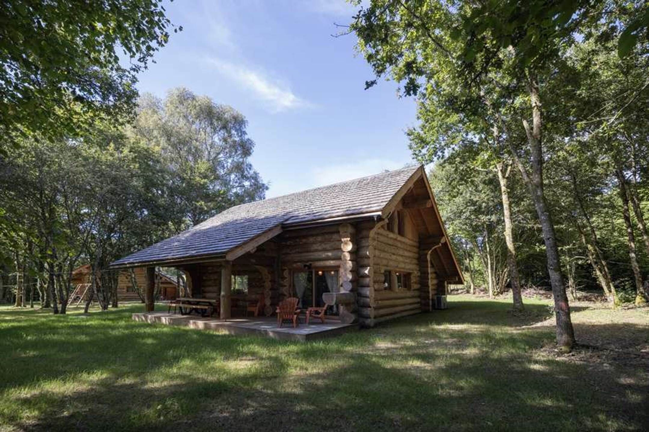 Une cabane en rondins avec un porche, entourée d’arbres.