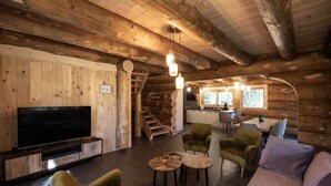 Interior de una cabaña de troncos con televisor, zona de estar, escalera y cocina.
