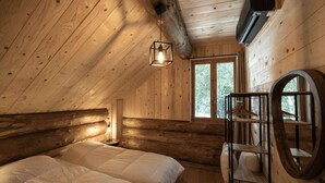 Un dormitorio rústico de cabaña de troncos con cama, lámpara colgante, ventana y espejo circular.