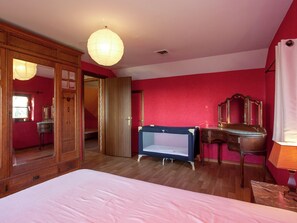 A bedroom with a large bed, a wooden wardrobe, a vanity with a mirror, and a hanging light fixture.