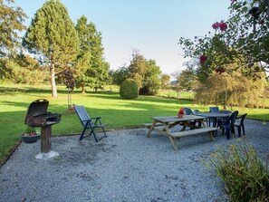 A patio area with a grill, seating, and a table, surrounded by trees and a well-maintained lawn.