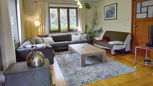 Ett mysigt vardagsrum med en soffgrupp, ett soffbord, en öppen spis och ett stort fönster med gardiner.