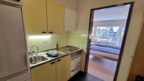 A compact kitchen with a sink, stove, and cabinets. A balcony with a bed is visible through an open door. - Haus Matten - Studio Findeln (Zermatt)
