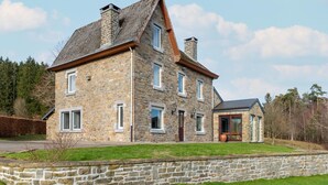 Une maison en pierre avec un toit à deux versants, de nombreuses fenêtres et une porte d’entrée.