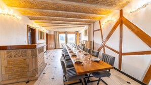 Une longue table à manger entourée de chaises, une cheminée en briques et un plafond en bois.