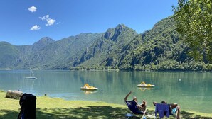 A lakeside view with two people relaxing on lawn chairs, a sailboat, and a small motorboat on the water. - Directly on the lake with terrace (Tre Capitelli)