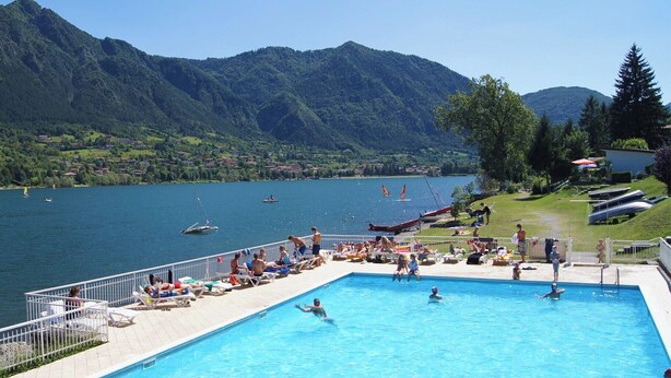 A swimming pool with people, a view of a lake, and mountains in the background. - Directly on the lake with terrace (Tre Capitelli)