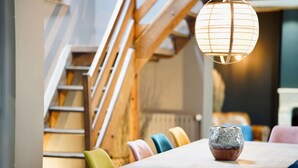 Un coin repas agrémenté d’un escalier en bois, de chaises colorées et d’une table sur laquelle est posé un vase décoratif.