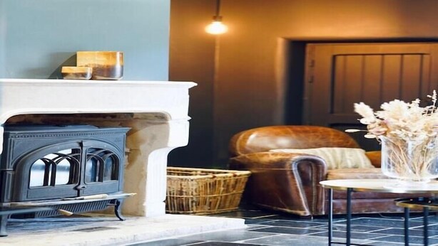 Un salon chaleureux avec une cheminée, un fauteuil en cuir, une petite table avec un vase et un panier.