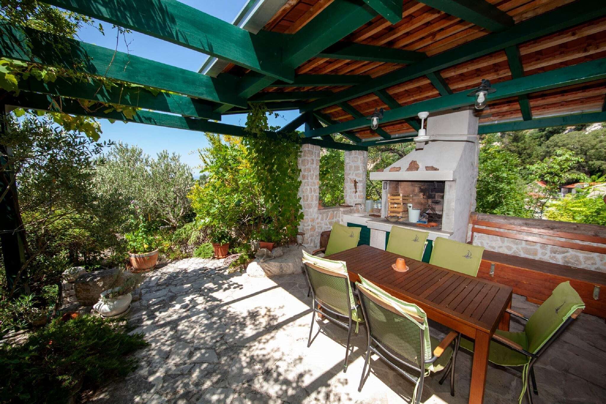 An outdoor patio with a stone table and chairs, a brick oven, and a stone wall.