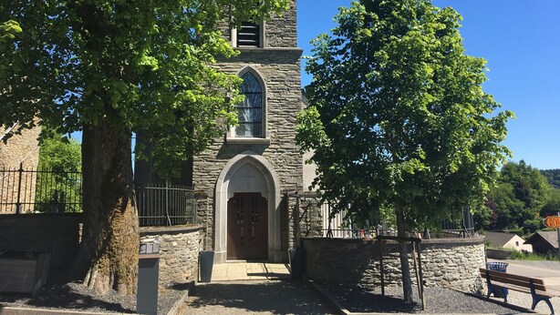 A stone church with a tall bell tower, arched entrance, and a large tree in front. - Family Apartment; Bouillon and Semois River (Gros-Fays)