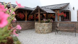 A courtyard with a stone planter, a wooden bench, and a pergola with hanging flower baskets. - Modern Spacious Holiday Home (Mettet (maison st Gérard))