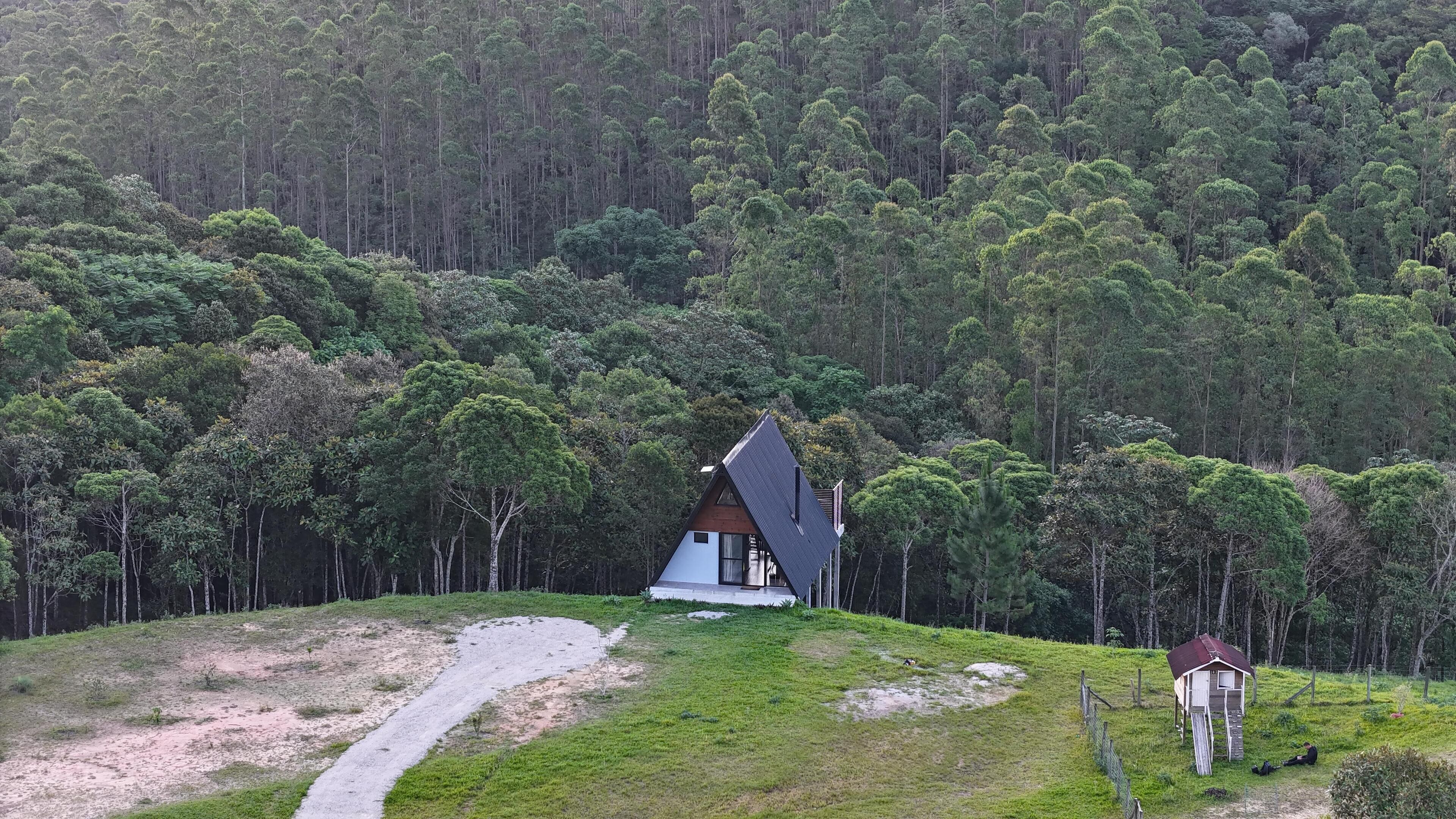 Une maison avec un toit en pente, entourée d’une forêt.