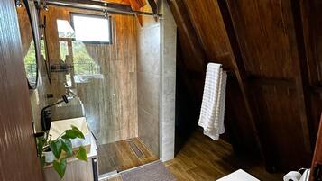 A compact, rustic bathroom with wooden beams, a shower, a toilet, and a sink with a plant.