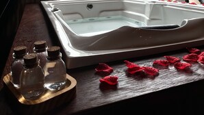 A hot tub with a wooden tray of bottles and rose petals, a window with a view of greenery, and a heart-shaped decoration. - Guiados Pelo Alto (Sao Pedro de Alcantara)
