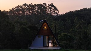 A modern A-frame cabin with a glass door entrance, surrounded by dense forest. - Guiados Pelo Alto (Sao Pedro de Alcantara)
