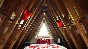 A cozy attic bedroom with a bed centered under a triangular window, surrounded by wooden beams and a sloped ceiling. - Guiados Pelo Alto (Sao Pedro de Alcantara)