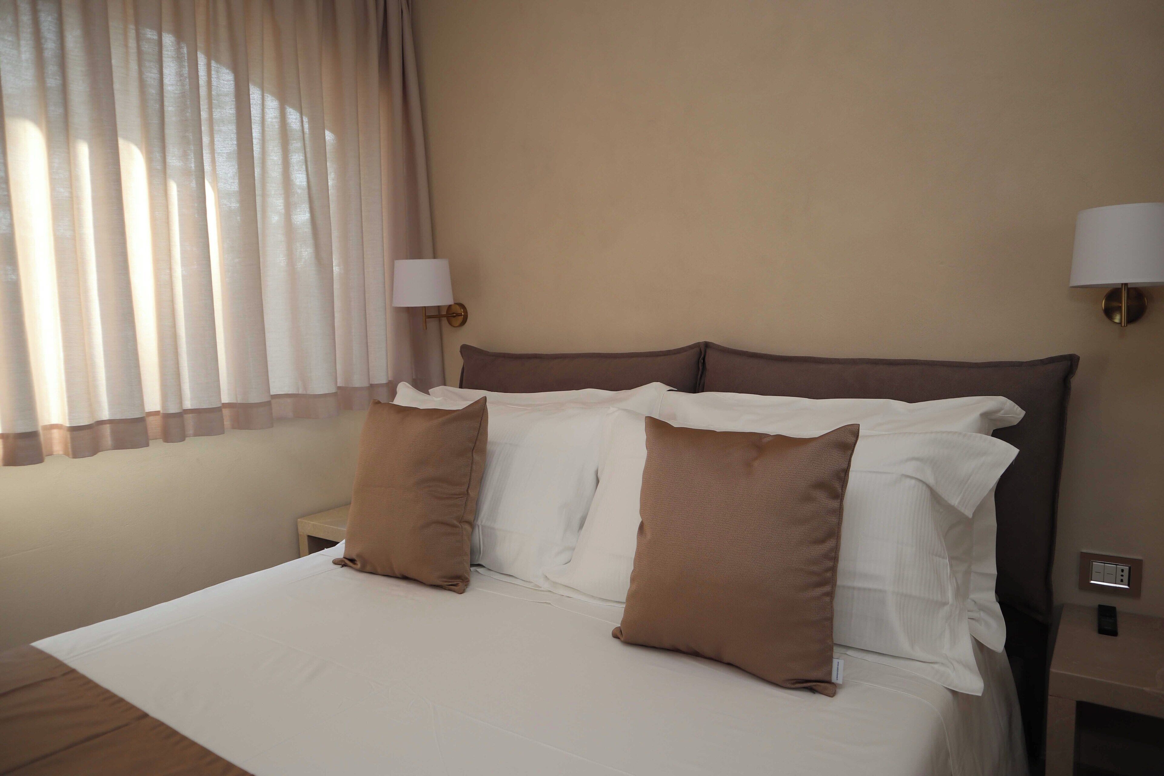 Ein Hotelzimmer mit einem großen Bett, zwei Nachttischlampen und einem Fenster mit Vorhängen.