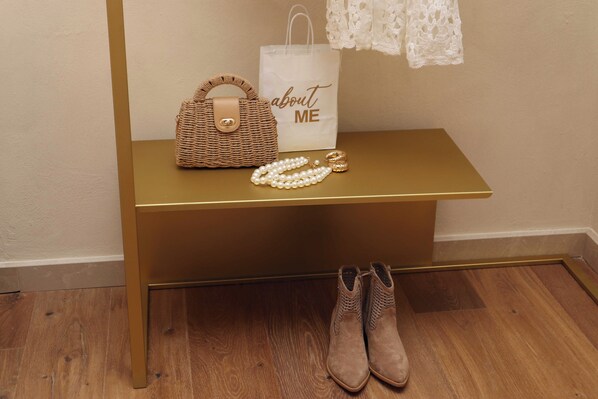A gold-colored bench with a woven handbag, pearl necklace, and a pair of boots on the floor.