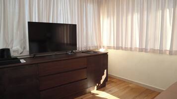 A room with a wooden dresser, a flat-screen TV, and sheer curtains.