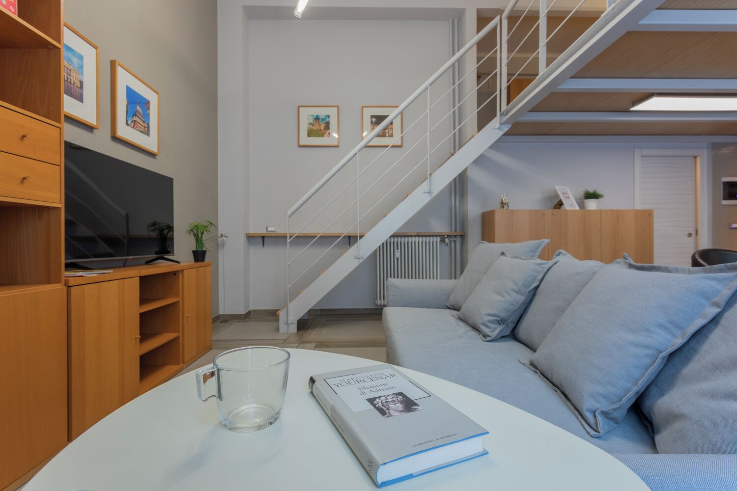 A modern living room with a staircase, a sofa, a coffee table, and a bookshelf.