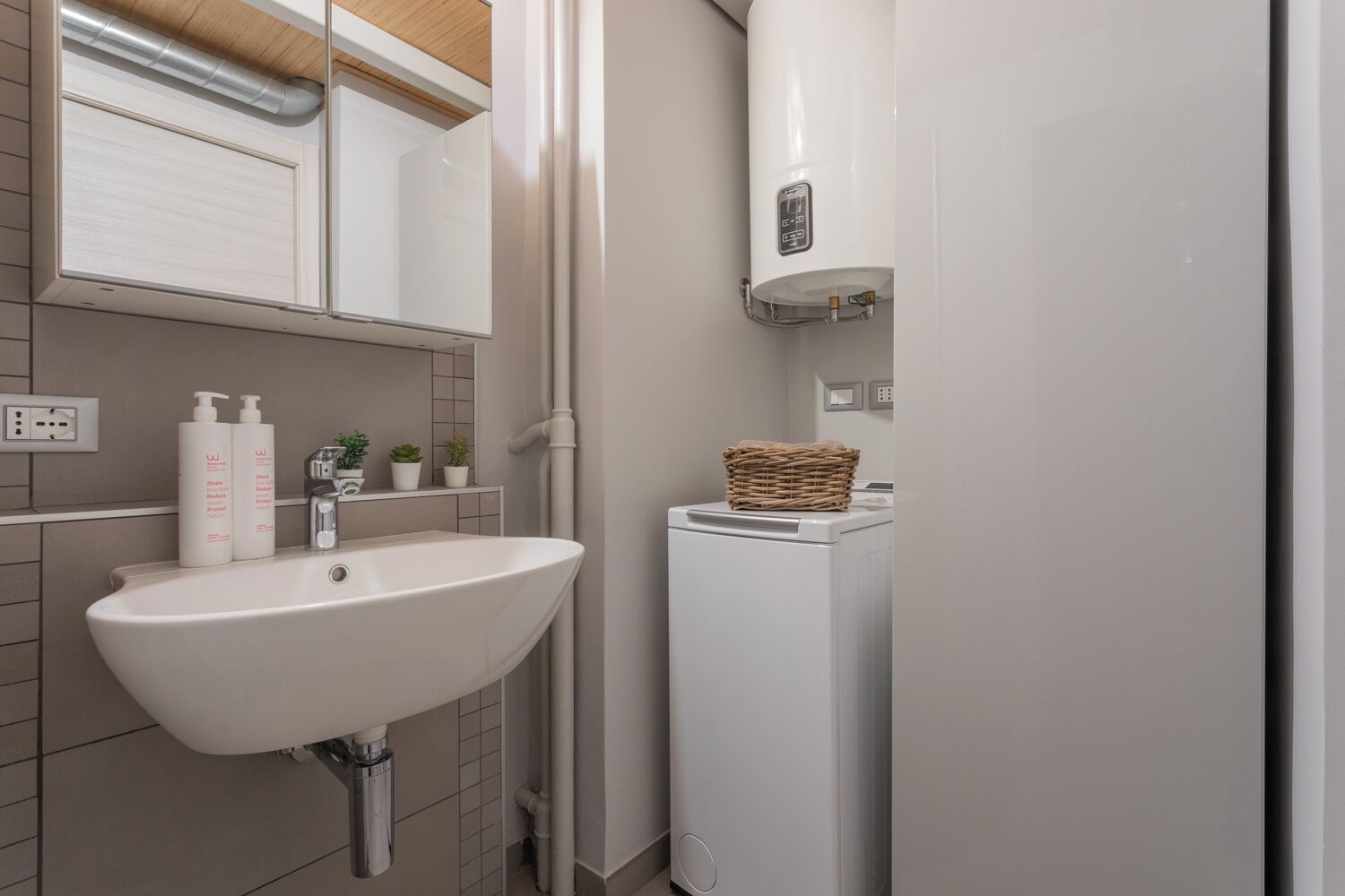 A bathroom with a white sink, a mirror, a towel rack, a washing machine, and a small shelf with toiletries.