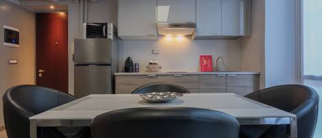 Een moderne keuken met witte kasten, een roestvrijstalen koelkast, een magnetron en een gasfornuis. Er staat een eettafel met twee zwarte stoelen en een kom op.
