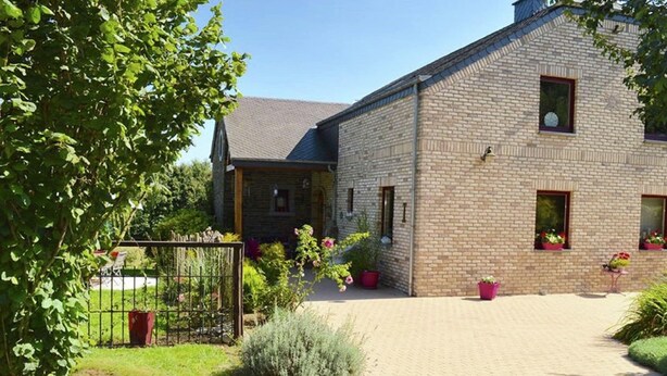 A two-story brick building with a paved driveway, surrounded by greenery and potted plants. - Cottage Oree des bois in Paliseul with garden (Paliseul)