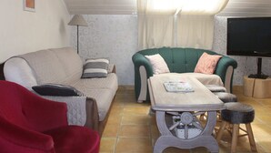A cozy living room with a sofa, a chair, a small table, and a television. - Cottage Oree des bois in Paliseul with garden (Paliseul)