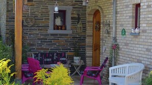 A stone building with a covered patio area featuring a wooden bench, a table, and two chairs. - Cottage Oree des bois in Paliseul with garden (Paliseul)